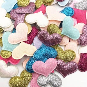 Könnte beinhalten: Eine Sammlung glitzernder herzförmiger Verzierungen in verschiedenen Farben, darunter rosa, blau, silber, gold und weiß. Die Herzen sind aus Filz und mit Glitzer bedeckt.