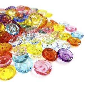 May include: Assortment of colorful, translucent plastic buttons in various shapes and sizes. The buttons have a shiny, glossy finish and are perfect for crafting projects.