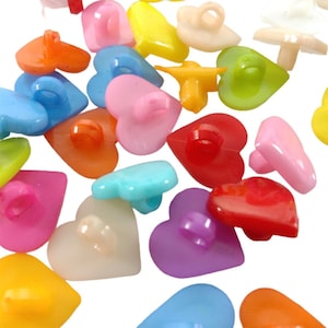 May include: Assortment of colourful plastic heart-shaped buttons with a loop for sewing. The buttons come in a variety of colours, including red, pink, blue, green, yellow, and orange.