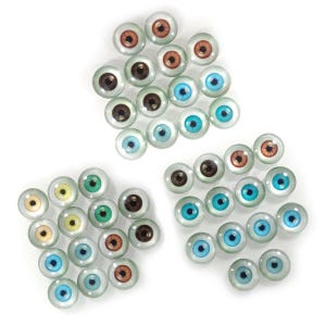 May include: Assortment of glass doll eyes in various colours, including blue, green, brown, and orange. The eyes are arranged in three groups on a white background.
