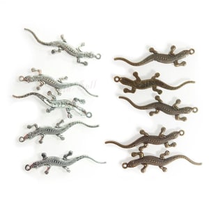 May include: A selection of metal lizard charms in silver and bronze hues. Each charm showcases a detailed lizard design with textured scales and a small loop for attachment. The charms are displayed against a white backdrop, ideal for crafting or jewellery making.