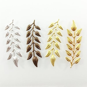 Peut inclure: Quatre brins de feuilles métalliques en argent, bronze et deux nuances d'or. Les brins sont disposés horizontalement sur un fond blanc.
