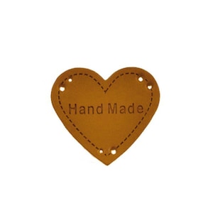 May include: Brown leather heart-shaped tag with the text "Hand Made" embossed on it. The tag has four holes punched through it.
