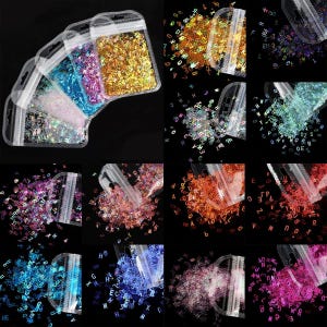 May include: Assortment of small plastic bags filled with iridescent holographic alphabet letter confetti. The bags are arranged in a grid pattern, with each bag containing a different colour of confetti.