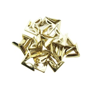 May include: A pile of gold-coloured metal corner protectors. The corner protectors are shaped like a right angle with a decorative design.