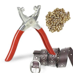 May include: A metal rivet setter tool with red handles, a pile of brass rivets, and a brown leather belt with silver hardware. The belt has a diamond pattern with silver eyelets.