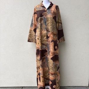 May include: A long-sleeved, floor-length robe featuring a full-length front zipper and a collar. The garment is decorated with a brown, tan, and gold abstract pattern of swirling lines and organic shapes throughout the entire fabric surface.