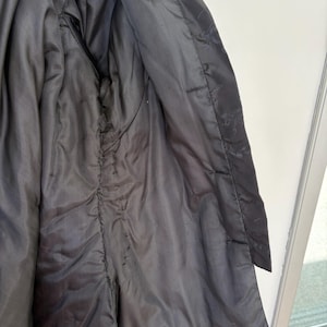 May include: Close-up of the inside of a black jacket. The lining is a shiny, dark fabric. The jacket's interior features a pocket and visible stitching along the seams. The outer fabric is a matte black.