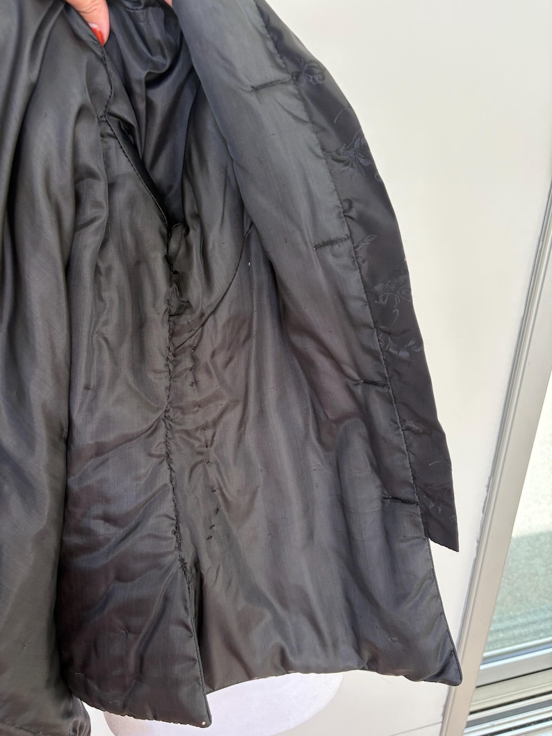 May include: Close-up of the inside of a black jacket. The lining is a shiny, dark fabric. The jacket's interior features a pocket and visible stitching along the seams. The outer fabric is a matte black.