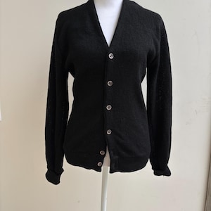 May include: A black cardigan sweater with a V-neck and long sleeves. The sweater has a button-up front with six round, silver-colored buttons. The cuffs and hem are ribbed. The sweater is displayed on a white mannequin.
