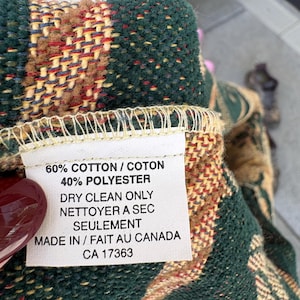 K&ouml;nnte beinhalten: Nahaufnahme eines gewebten Textils mit Etikett. Das Textil weist ein Muster aus Gr&uuml;n, Braun, Rot und Gelb auf. Das Etikett lautet: "60% COTTON / COTON, 40% POLYESTER, DRY CLEAN ONLY, MADE IN / FAIT AU CANADA, CA 17363."