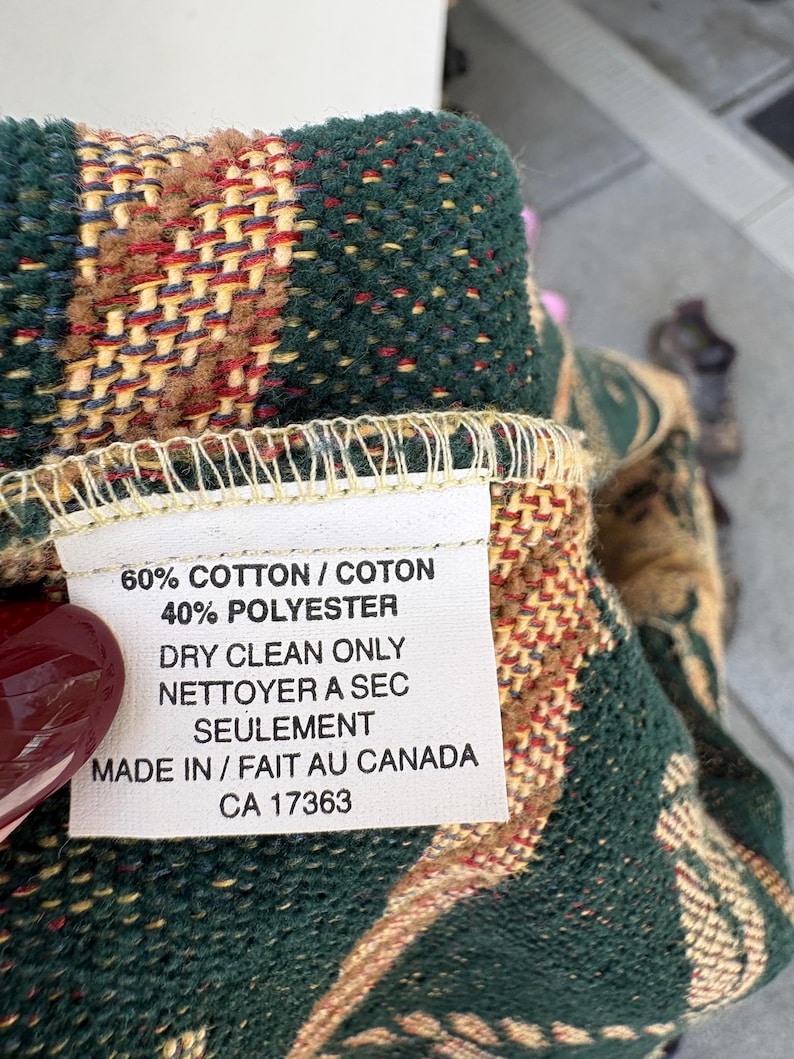 K&ouml;nnte beinhalten: Nahaufnahme eines gewebten Textils mit Etikett. Das Textil weist ein Muster aus Gr&uuml;n, Braun, Rot und Gelb auf. Das Etikett lautet: "60% COTTON / COTON, 40% POLYESTER, DRY CLEAN ONLY, MADE IN / FAIT AU CANADA, CA 17363."