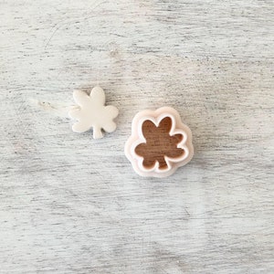 May include: Two plastic cookie cutters in the shape of a four-leaf clover. The larger cutter is pink and the smaller cutter is white.