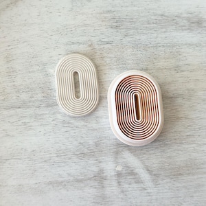 May include: Two white oval-shaped cookie cutters with concentric circles, one with a larger opening than the other.