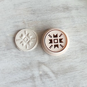 May include: Two round, white, ceramic stamps with a geometric design. The design on the left stamp is white on white, while the design on the right stamp is brown on white.