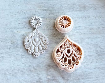 May include: Three beige polymer clay cutters in an overhead shot. One is a small circle with a sunburst design, another is a teardrop shape with an ornate floral design, and the third is a matching earring shape.