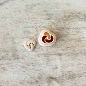 May include: Two white plastic cookie cutters in the shape of a three-leaf clover. The larger cutter has a brown center.