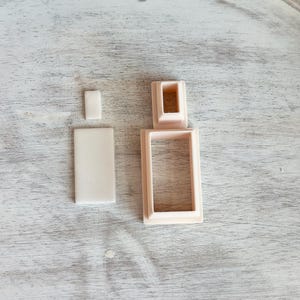 May include: A set of three plastic cookie cutters in the shape of a perfume bottle. The cutters are a light beige color.