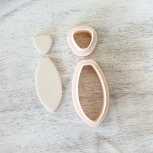 May include: A set of three cookie cutters in the shape of a leaf. The cutters are made of a light beige plastic and are arranged on a white wooden surface.