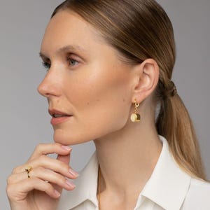 May include: Gold hoop earrings with a dangling round charm. The charm is a light beige color.