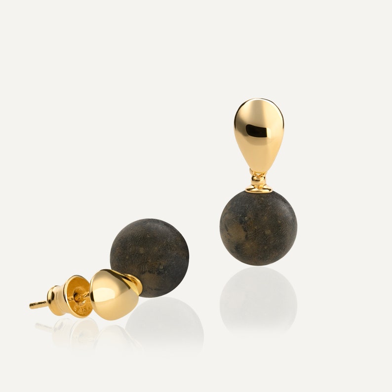 May include: A pair of gold and black earrings with a round, textured black stone and a gold teardrop-shaped top.