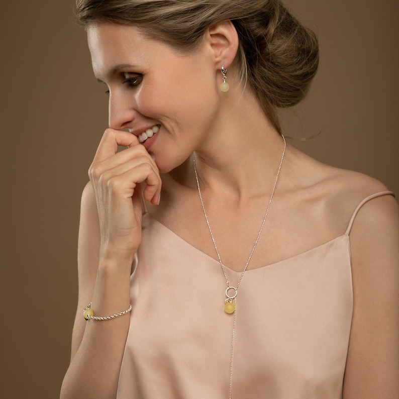 Model wearing lemon yellow matte amber pendant in 925 sterling silver with earrings and bracelet