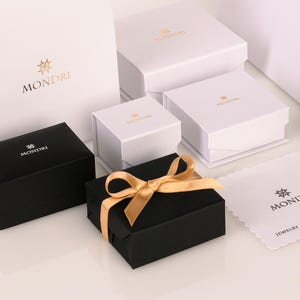 May include: A collection of white and black gift boxes with gold lettering that reads "MONDI" and a star logo. The boxes are arranged on a white surface. One box is tied with a gold ribbon.
