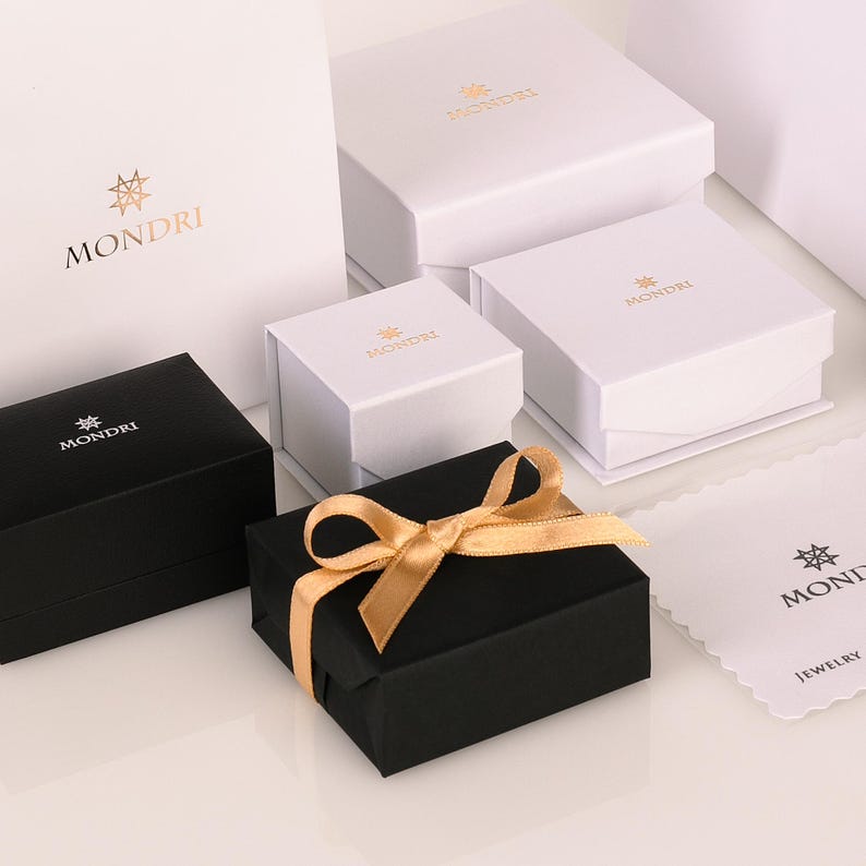 May include: A collection of white and black gift boxes with gold lettering that reads "MONDI" and a star logo. The boxes are arranged on a white surface. One box is tied with a gold ribbon.