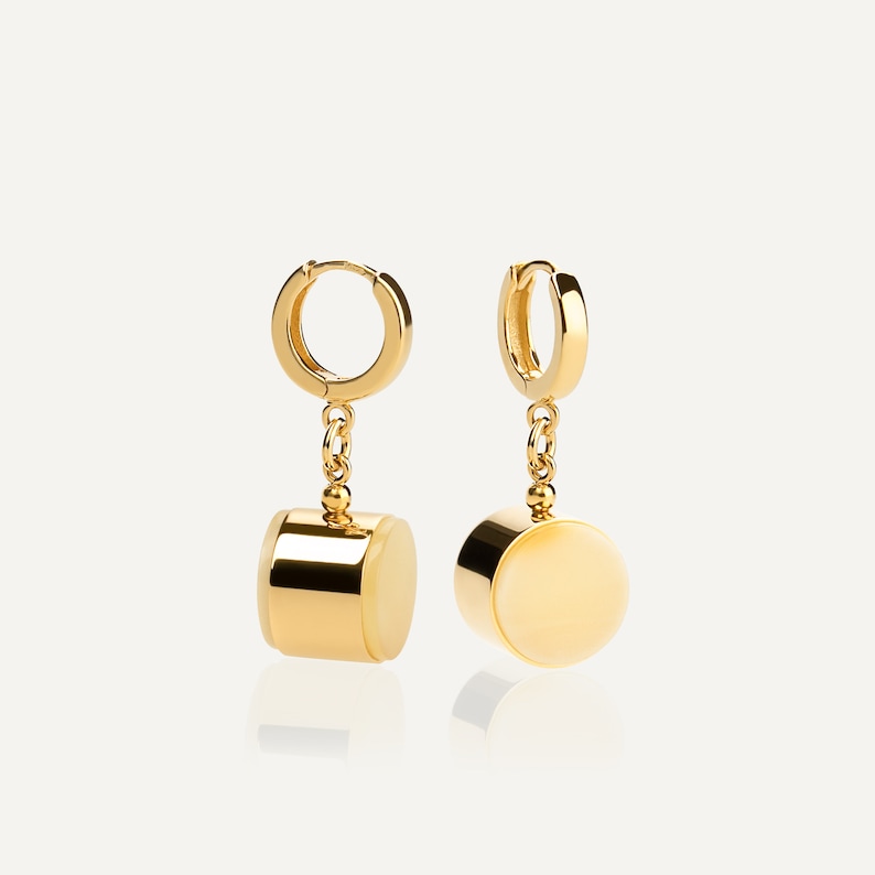 May include: A pair of gold hoop earrings with a dangling round, off-white stone and a gold cylinder charm.