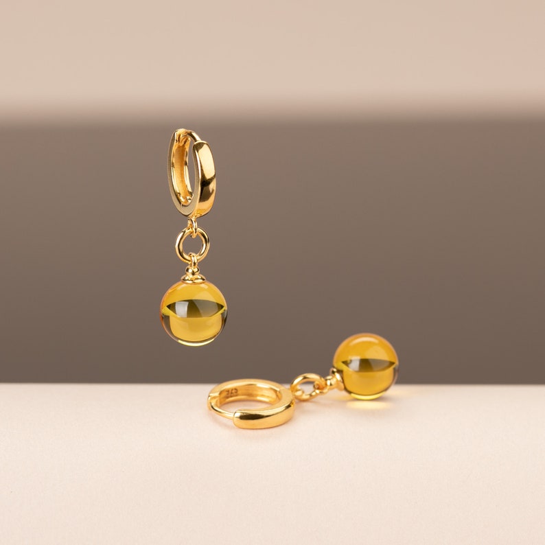 May include: A pair of gold hoop earrings with a dangling amber sphere. The earrings are simple and elegant.