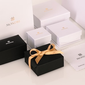 May include: A set of five black and white gift boxes with a gold star logo that says "MONDRI". The boxes are arranged in a pyramid shape with a gold ribbon on the top box.