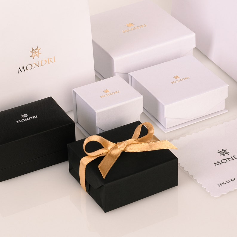 May include: A set of five black and white gift boxes with a gold star logo that says "MONDRI". The boxes are arranged in a pyramid shape with a gold ribbon on the top box.