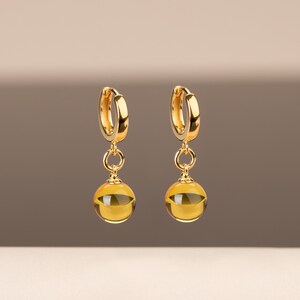 May include: A pair of gold hoop earrings with a dangling amber-colored sphere attached to each hoop.