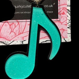 May include: A turquoise glitter music note pendant necklace with a silver chain. The pendant is black outlined and has a sparkly finish.