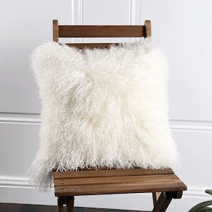 Peut inclure: Un coussin en peau de mouton blanc et moelleux posé sur une chaise en bois. Le coussin est doux et moelleux, parfait pour ajouter une touche de luxe à n'importe quelle pièce.