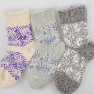 May include: Three pairs of wool socks with different patterns. One pair is white with a purple snowflake design, one pair is light blue with a white snowflake design, and one pair is gray with a white snowflake design.