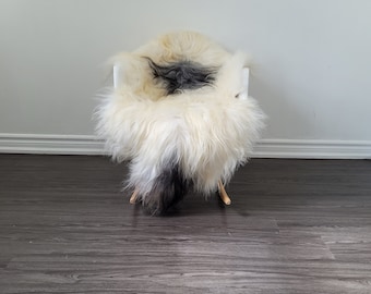 Può includere: Un tappeto di pelle di pecora bianca con accenti neri è drappeggiato su una sedia bianca. La sedia è su un pavimento di legno scuro.
