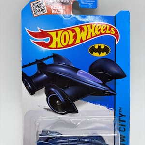 May include: A Hot Wheels toy car in a dark blue Batmobile design, packaged on a blue and white card. The card features the Hot Wheels logo, a Batman symbol, and the text "HW City". The car is a die-cast model.