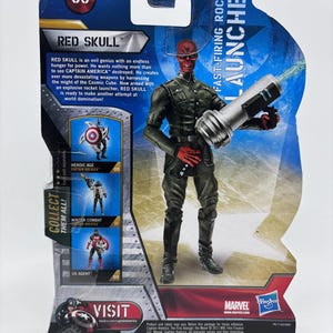 May include: Red Skull action figure on a Marvel branded card. The figure is in a combat pose, holding a silver and black rocket launcher. The card features text including "Red Skull" and "Fast-Firing Rocket Launcher."