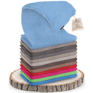 Könnte beinhalten: Ein Stapel von 10 Kaschmirschals in verschiedenen Farben, darunter Blau, Grau, Braun, Rot, Rosa, Grün und Hellblau. Der oberste Schal ist gefaltet und hat ein Etikett mit der Aufschrift "feinstes Kaschmir" in deutscher Sprache. Die Schals werden auf einer Holzscheibe präsentiert.