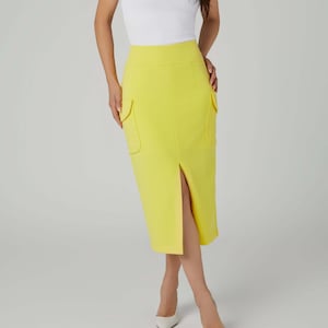 May include: A woman's outfit featuring a white ribbed tank top and a bright yellow pencil skirt with front pockets and a front slit. The woman is wearing white heels. The outfit is set against a plain white background.