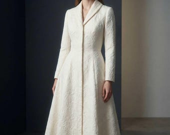 May include: A long, ivory-colored coat dress with a textured floral pattern. The dress features a notched collar, long sleeves, and a button-down front. The skirt flares out from the waist, creating a classic silhouette.