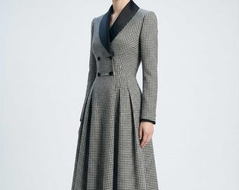 May include: A long-sleeved houndstooth dress with a black satin lapel and double-breasted button closure. The dress features a fitted bodice and a pleated skirt, creating a classic silhouette. The dress is in black and white.