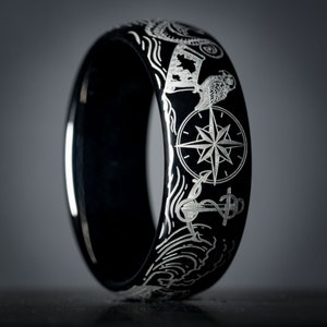 May include: A black ring with a silver compass, anchor, and waves design.