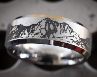 May include: A silver ring with a mountain range engraved on the top. The ring is made of stainless steel and has a brushed finish.