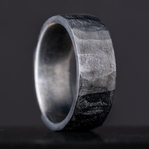 May include: A silver ring with a hammered finish. The ring is wide and has a textured surface.