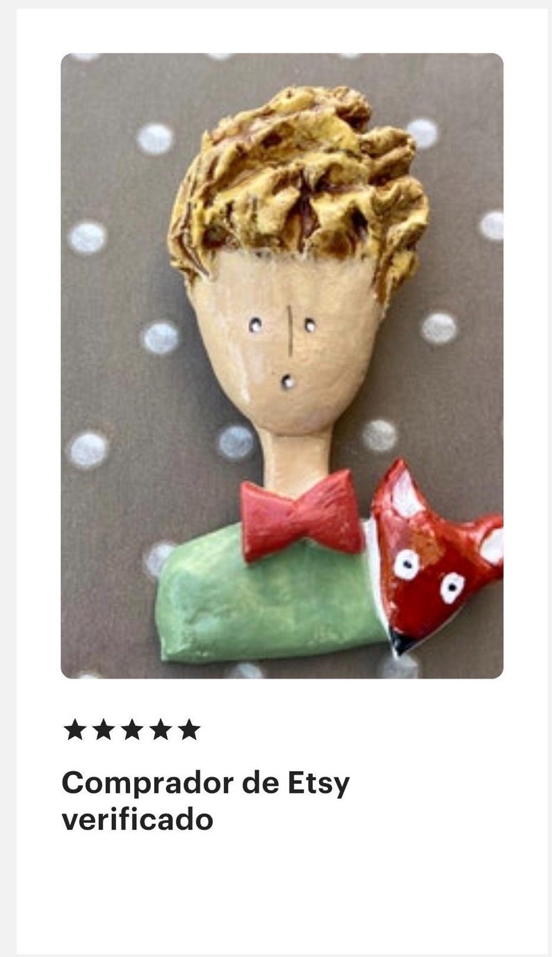 May include: A sculpted brooch featuring a figure with textured yellow hair, a pale face, and a small mouth. The figure wears a green shirt with a red bow tie and is accompanied by a small red fox with white eyes positioned on the right shoulder.