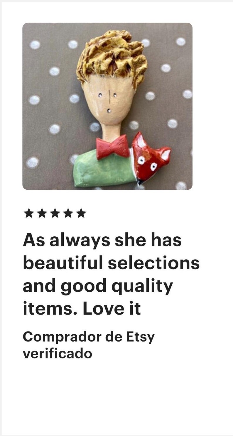 May include: A handcrafted brooch featuring a stylized figure with textured golden-brown hair, a pale face, a red bow tie, and a light green shirt. A small red fox with white accents is positioned next to the figure, resting against the green shirt.