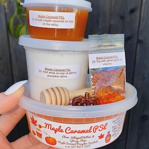 May include: A Maple Caramel PSL slime kit in a 236 ml container, including a white whipped slime, an orange glossy slime, a small bag of glitter, a wooden honey dipper, and a small brown pumpkin charm, with instructional labels on each container.