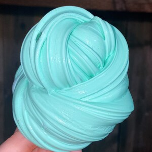 May include: A close-up of a light blue slime, with a smooth, glossy texture. The slime is folded and twisted into a ball shape.